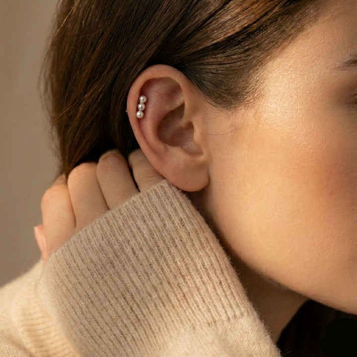 Close-up of an ear with a pearl earring, wearing a beige sweater.