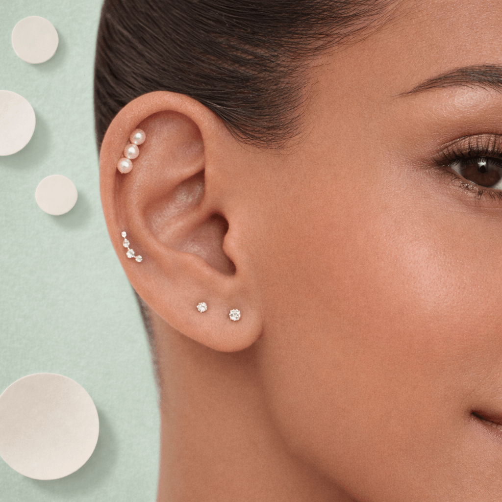 Close-up of a woman's ear with multiple earrings against a light green background with circular patterns.