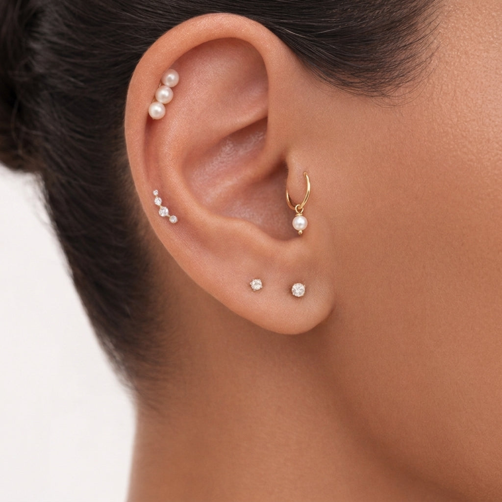 Close-up of an ear with multiple pearl earrings on a neutral background