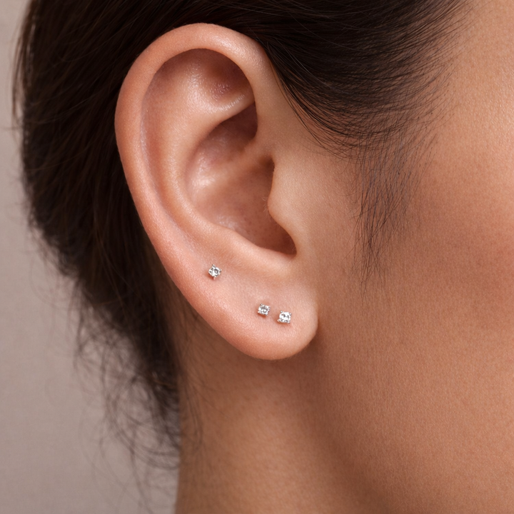 Close-up of an ear wearing three small diamond stud earrings with a neutral background