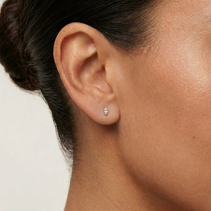 Close-up of an ear wearing a small marquise CZ earring on a neutral background